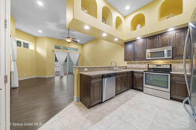 kitchen featuring ceiling fan, sink, light stone counters, kitchen peninsula, and appliances with stainless steel finishes