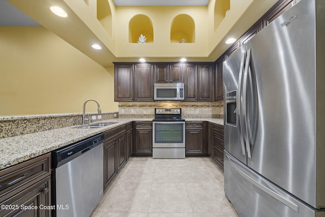 kitchen with light stone countertops, appliances with stainless steel finishes, a towering ceiling, sink, and light tile patterned floors