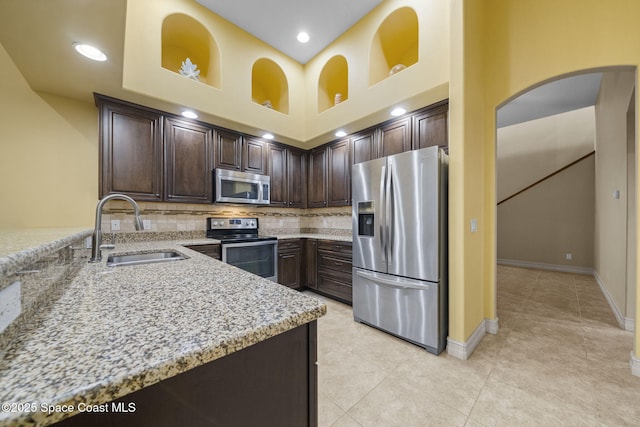 kitchen featuring dark brown cabinets, light stone countertops, sink, and appliances with stainless steel finishes