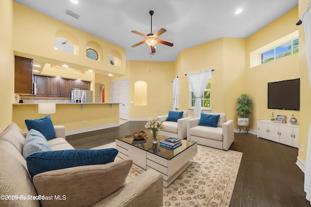 living room featuring dark hardwood / wood-style floors, ceiling fan, and a towering ceiling