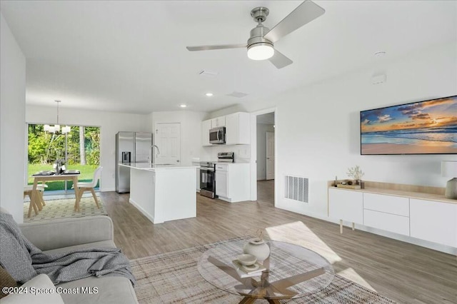 living room with hardwood / wood-style floors, ceiling fan with notable chandelier, and sink