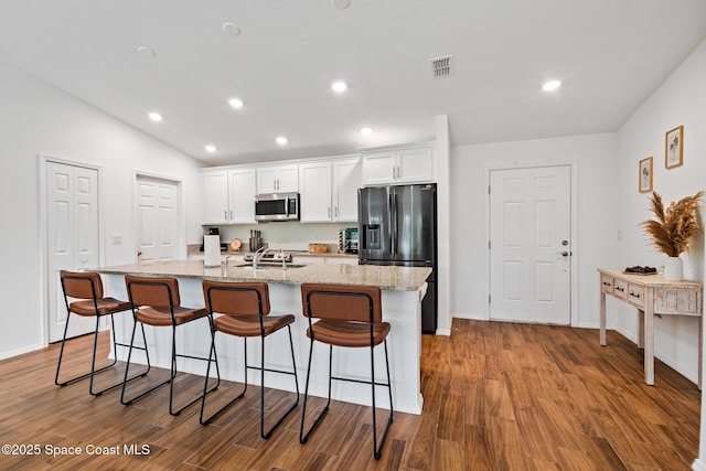 kitchen with a kitchen breakfast bar, hardwood / wood-style floors, a center island with sink, white cabinets, and appliances with stainless steel finishes