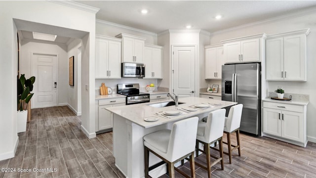 kitchen with white cabinets, a center island with sink, sink, appliances with stainless steel finishes, and a breakfast bar area