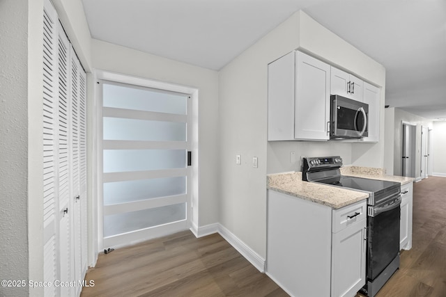 kitchen with black electric range, hardwood / wood-style floors, white cabinetry, and light stone counters