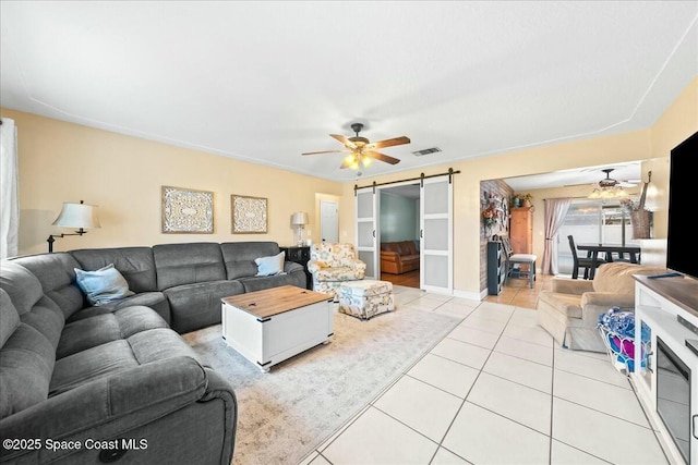 living room featuring a barn door, ceiling fan, and light tile patterned flooring