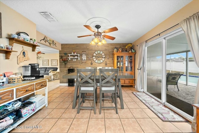 dining area with a textured ceiling, wood walls, ceiling fan, and light tile patterned floors