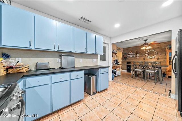 kitchen featuring wood walls, stove, blue cabinets, ceiling fan, and fridge