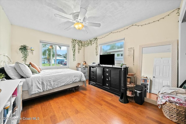 bedroom with ceiling fan, wood-type flooring, a textured ceiling, and multiple windows