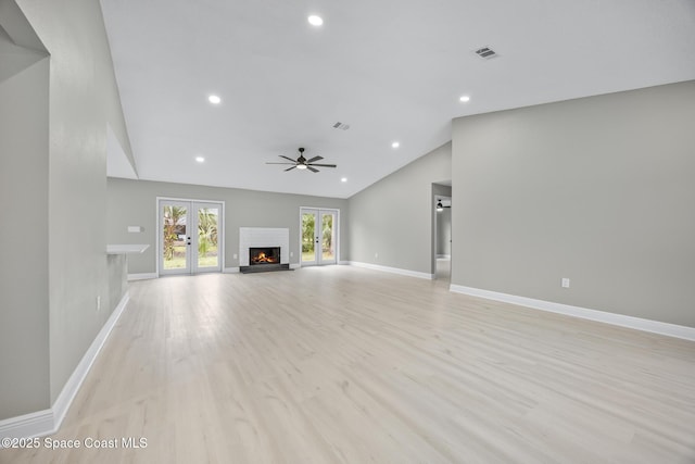 unfurnished living room featuring lofted ceiling, french doors, a brick fireplace, ceiling fan, and light wood-type flooring