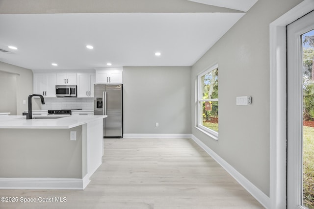 kitchen featuring light wood-type flooring, tasteful backsplash, stainless steel appliances, sink, and white cabinets