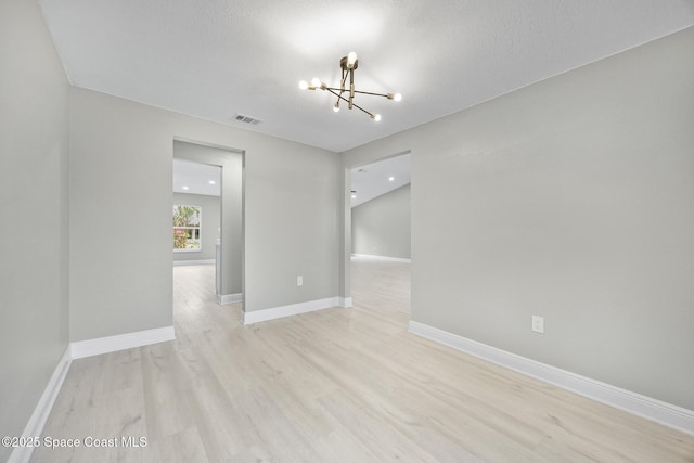 unfurnished room with a notable chandelier, a textured ceiling, and light hardwood / wood-style flooring