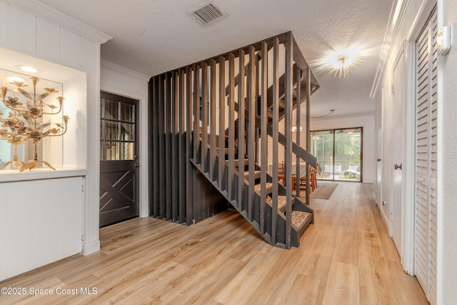 stairs with wood-type flooring, ornamental molding, and a textured ceiling