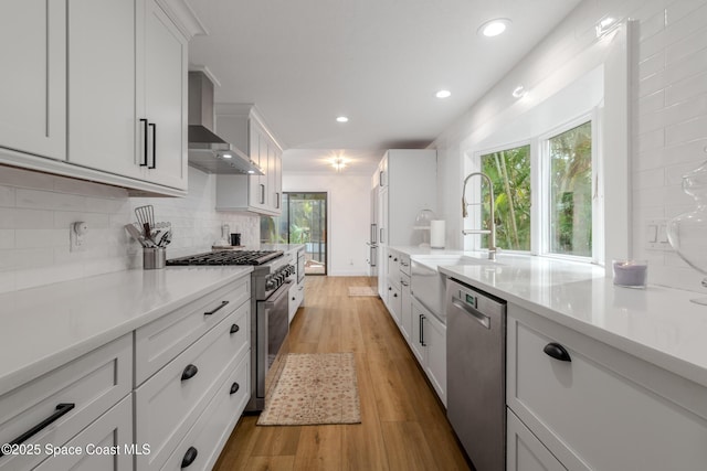 kitchen with sink, wall chimney exhaust hood, white cabinetry, light hardwood / wood-style floors, and stainless steel appliances