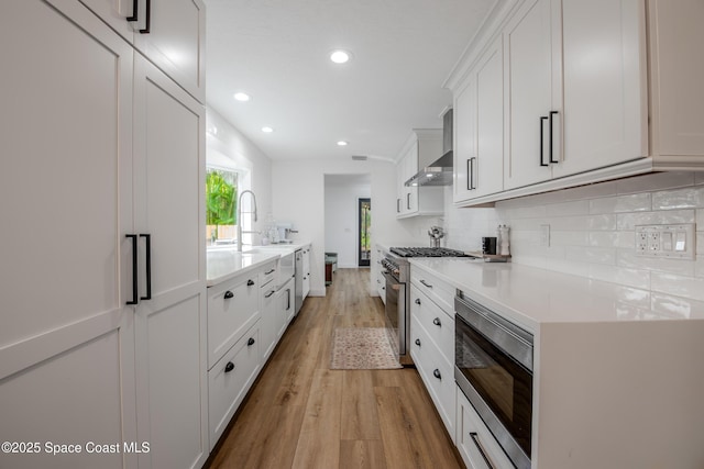 kitchen featuring white cabinets, wall chimney range hood, stainless steel appliances, decorative backsplash, and light hardwood / wood-style flooring