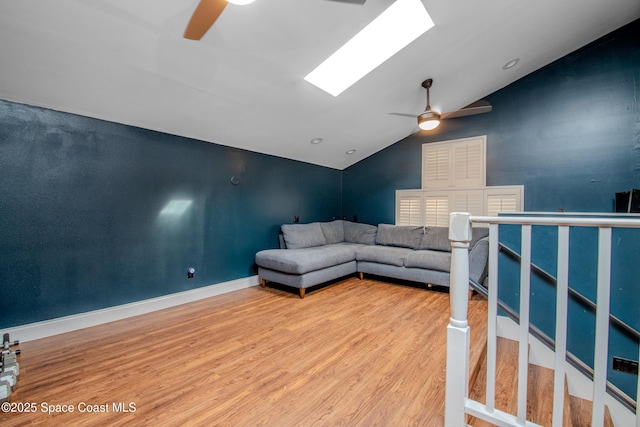 living room with ceiling fan, vaulted ceiling with skylight, and wood-type flooring