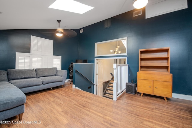 living room featuring wood-type flooring, ceiling fan, high vaulted ceiling, and a skylight