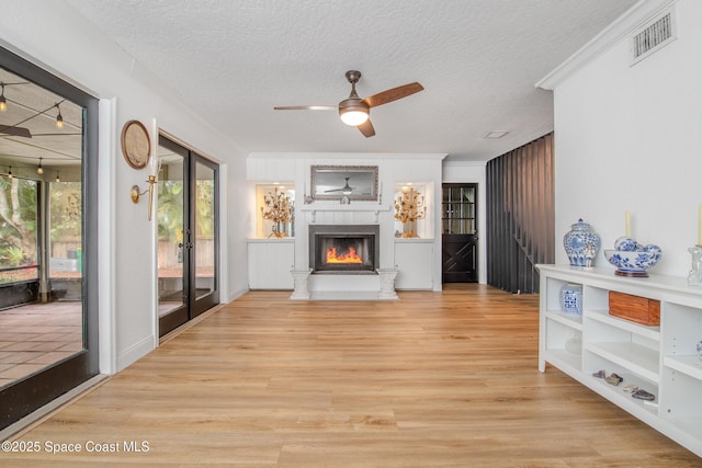 living room featuring a textured ceiling, a large fireplace, light hardwood / wood-style flooring, ornamental molding, and ceiling fan