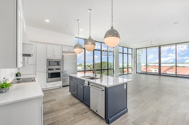 kitchen featuring a center island with sink, white cabinetry, a wall of windows, and appliances with stainless steel finishes