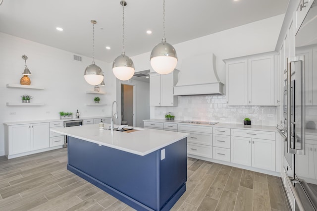 kitchen featuring pendant lighting, premium range hood, white cabinetry, and sink