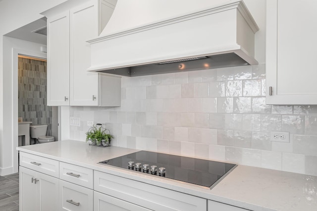 kitchen featuring decorative backsplash, white cabinetry, black electric stovetop, and custom exhaust hood