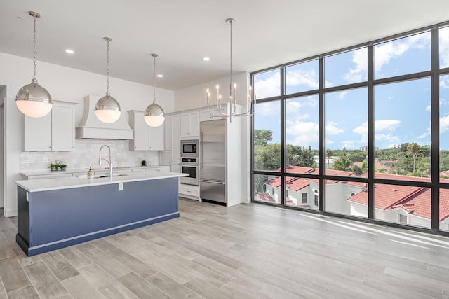 kitchen featuring premium range hood, built in appliances, expansive windows, and decorative light fixtures