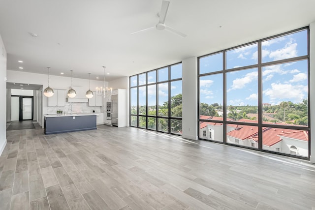 unfurnished living room featuring ceiling fan with notable chandelier, expansive windows, and light wood-type flooring