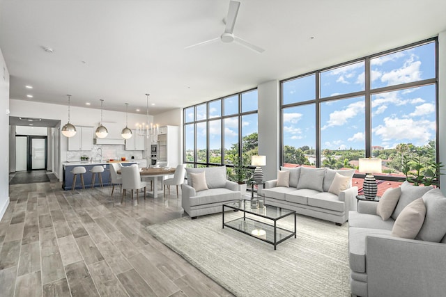 living room featuring ceiling fan with notable chandelier, light hardwood / wood-style floors, a wall of windows, and sink