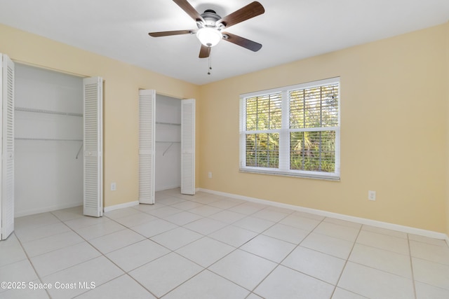 unfurnished bedroom featuring light tile patterned floors, ceiling fan, and multiple closets