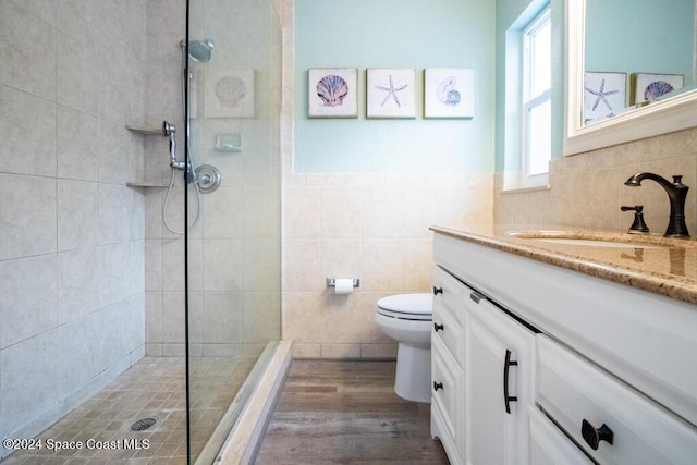 bathroom featuring vanity, hardwood / wood-style flooring, toilet, tile walls, and a tile shower