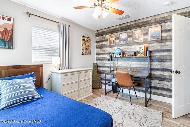 bedroom featuring wood walls, ceiling fan, a textured ceiling, and light wood-type flooring