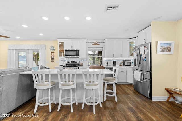 kitchen with white cabinetry, dark wood-type flooring, backsplash, a kitchen bar, and appliances with stainless steel finishes