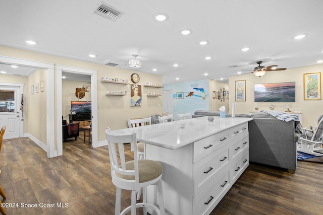 kitchen with dark wood-type flooring, white cabinets, a kitchen breakfast bar, ceiling fan, and kitchen peninsula