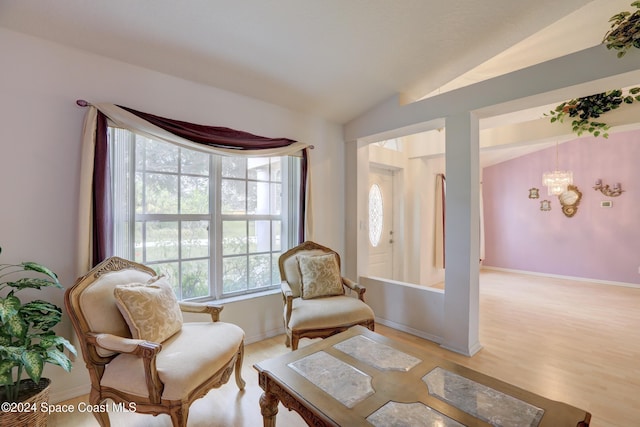 living area featuring a chandelier, light hardwood / wood-style flooring, vaulted ceiling, and a healthy amount of sunlight