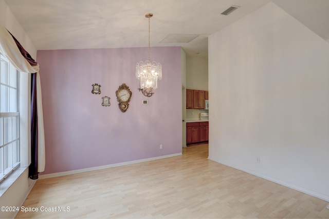 unfurnished room with a notable chandelier, light wood-type flooring, and a wealth of natural light