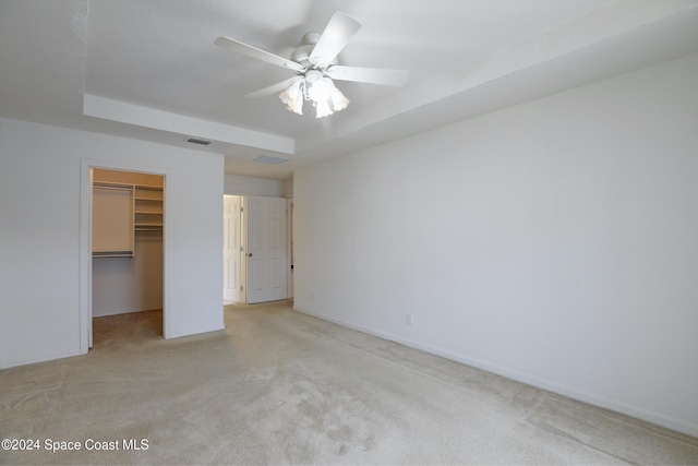 unfurnished bedroom featuring a walk in closet, a tray ceiling, light colored carpet, ceiling fan, and a closet