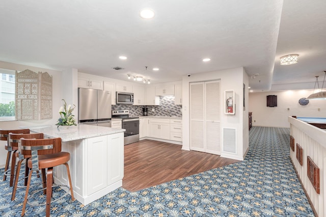 kitchen with kitchen peninsula, decorative backsplash, appliances with stainless steel finishes, light stone counters, and white cabinetry