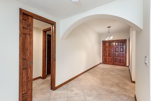 hallway featuring light tile patterned floors, a textured ceiling, and a notable chandelier