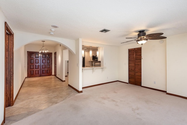 carpeted spare room featuring a textured ceiling and ceiling fan with notable chandelier