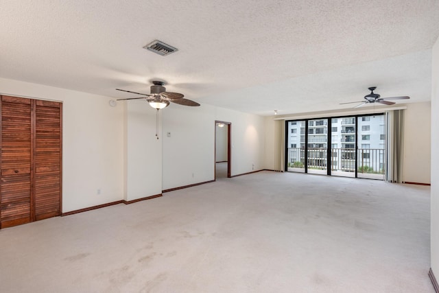 spare room with a textured ceiling, light colored carpet, and ceiling fan