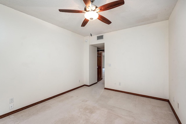 spare room featuring ceiling fan, light colored carpet, and a textured ceiling