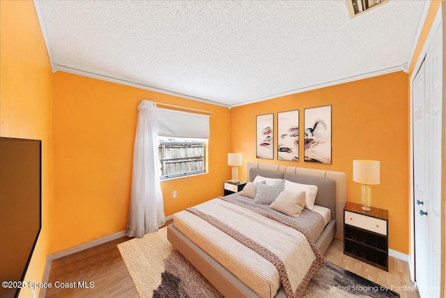 bedroom featuring a textured ceiling, light wood-type flooring, a closet, and ornamental molding