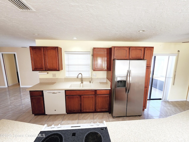 kitchen featuring dishwasher, sink, light tile patterned floors, a textured ceiling, and stainless steel fridge with ice dispenser