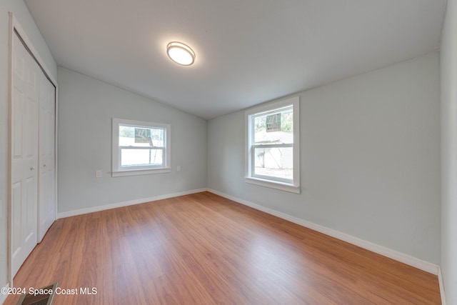 unfurnished bedroom featuring light hardwood / wood-style floors, multiple windows, and a closet