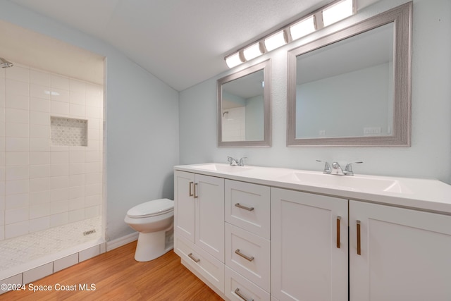 bathroom with tiled shower, hardwood / wood-style floors, vanity, and toilet