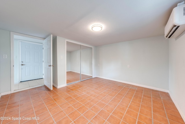 unfurnished bedroom with a closet, light tile patterned floors, a textured ceiling, and a wall mounted AC