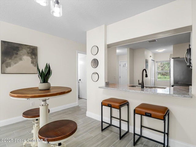 kitchen featuring light stone countertops, sink, a kitchen breakfast bar, kitchen peninsula, and stainless steel fridge