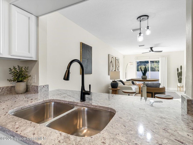 room details featuring light stone counters, sink, white cabinets, and ceiling fan