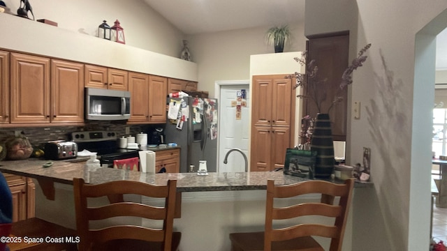 kitchen featuring a kitchen breakfast bar, appliances with stainless steel finishes, tasteful backsplash, stone countertops, and kitchen peninsula