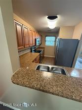 kitchen featuring black fridge, sink, stainless steel range oven, light stone counters, and kitchen peninsula