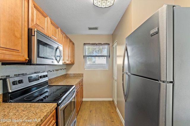 kitchen featuring backsplash, light hardwood / wood-style flooring, a textured ceiling, and appliances with stainless steel finishes